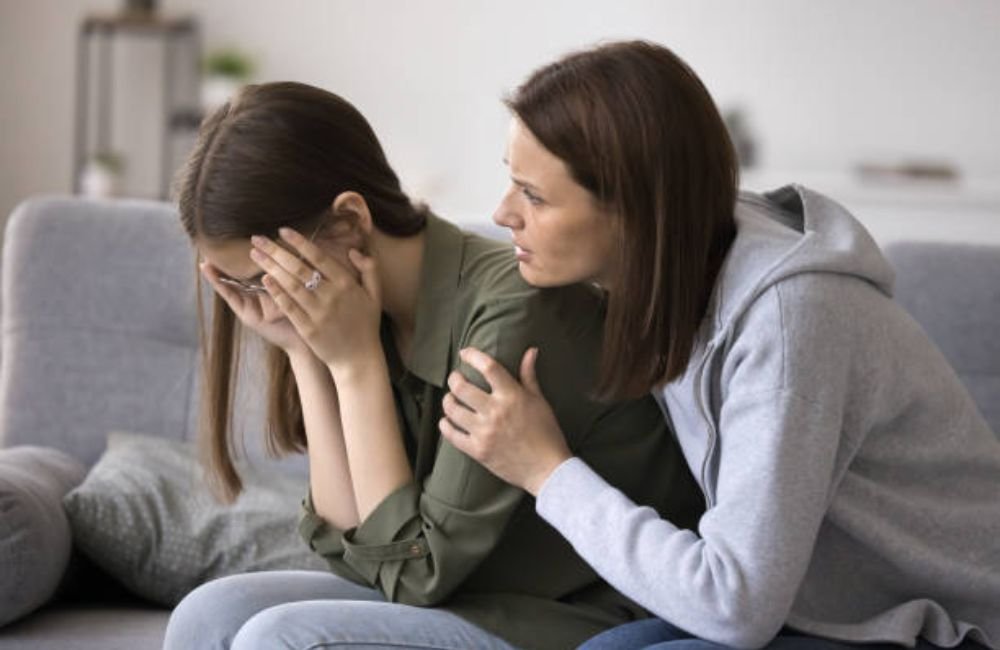 Woman comforting another woman who is covering her face in distress