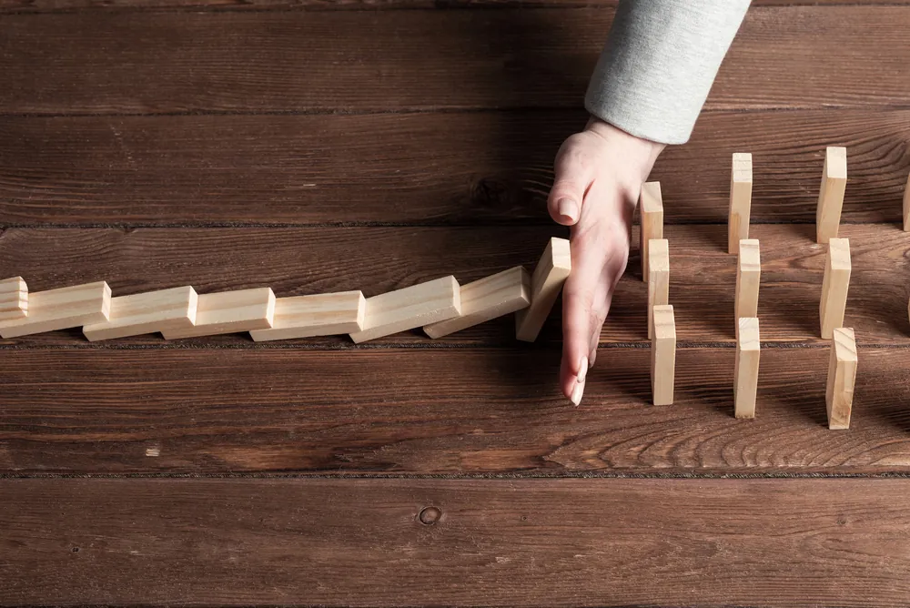 Hand stopping a row of falling wooden blocks, representing crisis stabilization