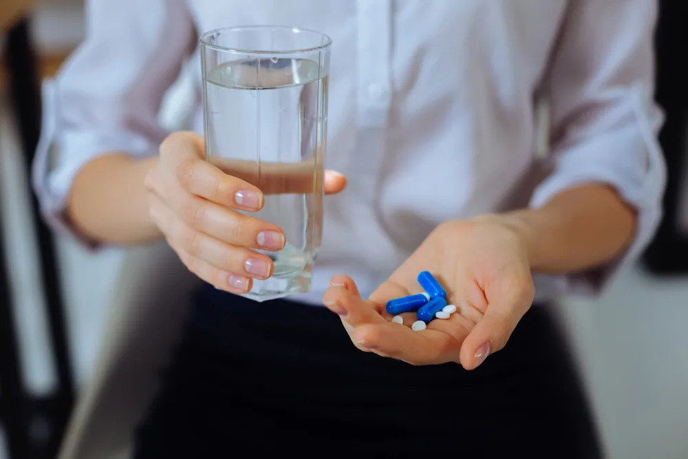 Person holding water and prescribed pills, representing daily medication management