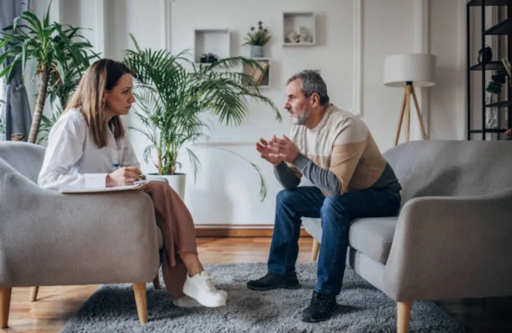 Man gesturing while a therapist takes notes during a mental health session