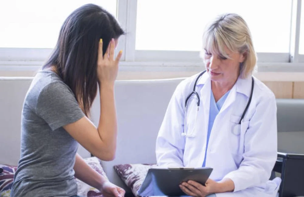 Distressed woman beside a doctor reviewing notes on a tablet during a dual diagnosis evaluation